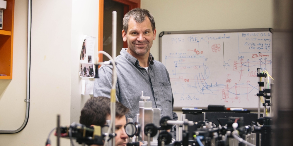 Austin Roorda standing with an adaptive optics scanning laser ophthalmoscope.