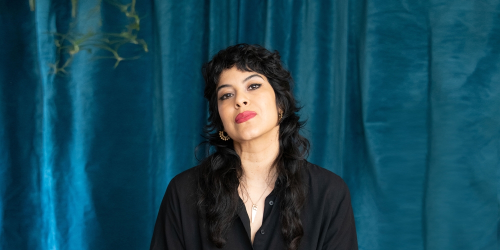 A person with long wavy black hair sits facing forward