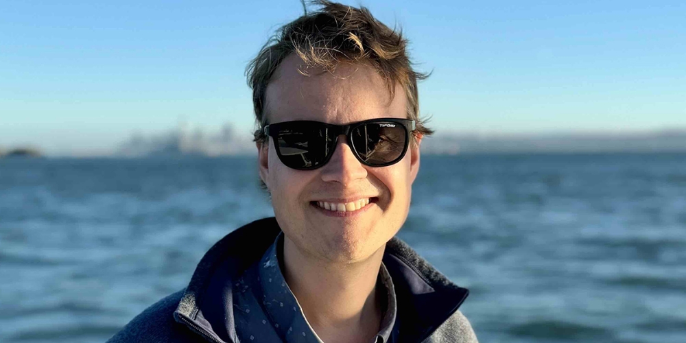 person with dark glasses standing with water in background