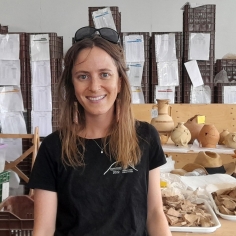 Photo of Grace Erny in front of table with archaeological ceramics