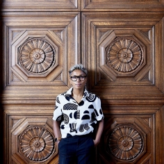 Poulomi Saha standing in front of decorative wood panels, hands in pockets