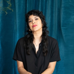 A person with long wavy black hair sits facing forward