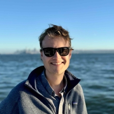 person with dark glasses standing with water in background