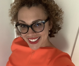 woman with black glasses, curly hair wearing orange dress