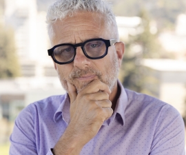 person with short gray hair and black rim glasses holding chin
