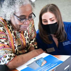 Older woman and younger woman wearing a mask looking together at a printed document and computer screen.