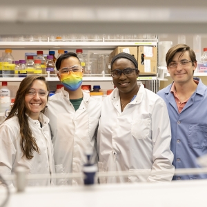Four people standing in a lab, some wearing lab coats and masks