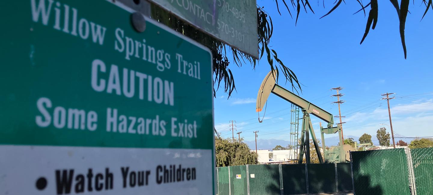 A photo shows an oil rig located in a neighborhood in Los Angeles. In the foreground is a sign for a city park.