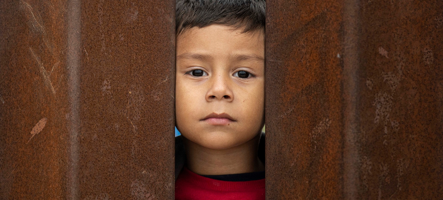a young child looking through two bars of the wall between the US and Mexico