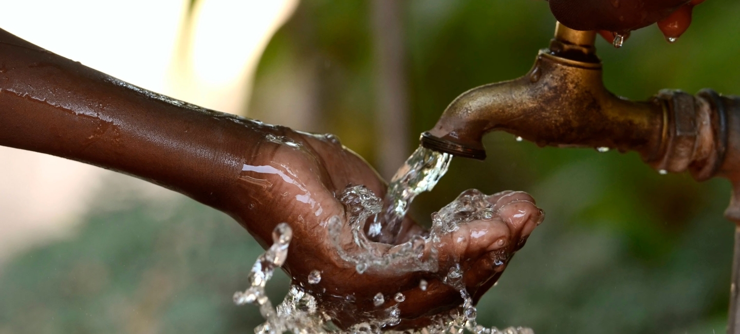 Child's hand receiving water from a spigot.