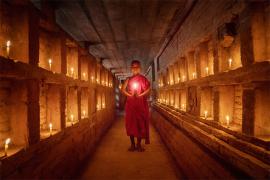 Buddhist monk standing in the middle of a corridor lit with candles
