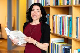 A photo of Jennifer Tour Chayes holding a book on computer programming in front of a bookshelf