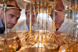 three researchers gather around gold-colored ultracold freezer