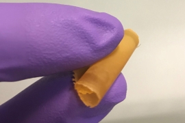 gloved fingers holding a rolled polymer membrane