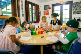 young children in a colorfully decorated classroom with a mask-wearing teacher