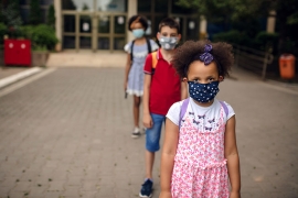 three young students, masked and socially distanced, await the start of a school day