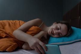 Teenage girl lies in bed and smiles as she looks at electronic device