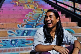 Jesus Nazario, a Ph.D. student in ethnic studies, sitting on a colorful outdoor stairway and smiling.