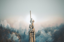 a steel statue of a person holding a sword with trees and fog in the background