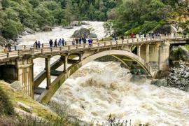people standing on bridge looking at raging floodwaters