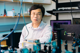 Ke Yu sitting in lab with instrumentation in the foreground.