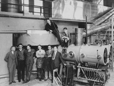 8 people standing in a line next to the 60-inch cyclotron, Ernest Lawrence being the third person from the left 