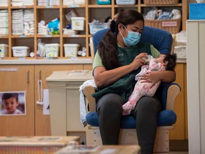 Woman wearing anti-virus mask feeds infant in a day-care setting