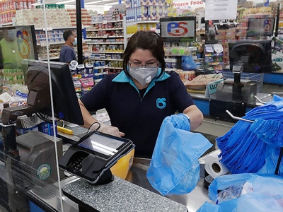 A retail checkout clerk, masked against coronavirus infection, puts purchases into blue plastic bags