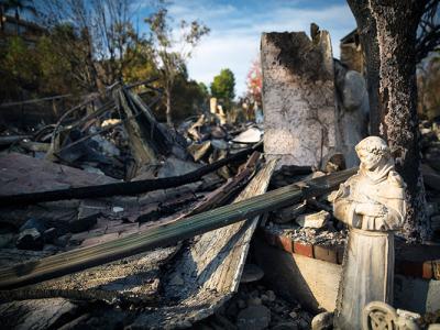 A photo of burned wreckage following a wildfire, with a small ceramic figure out a saint in the foreground.