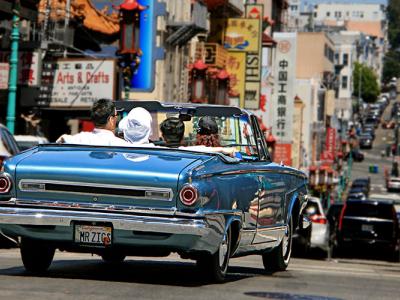 A classic convertible automobile, full of people, driving down a street in San Francisco's Chinatown district