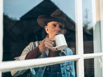 Old man with coffee cup staring out of window.