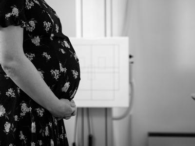 A black and white photo shows the profile of a pregnant person holding their belly.
