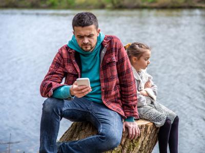 Adult frowning at smartphone while child sits with arms folded.