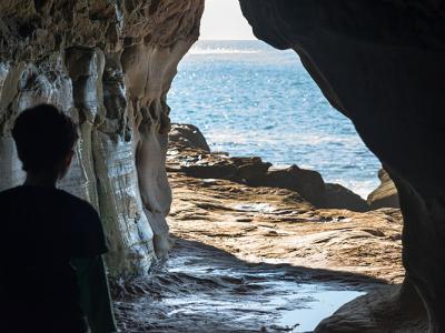A child looking out from a cave at the ocean.