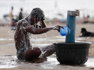 On a day of scorching temperatures, a man in India sits and drenches himself in water from a public fountain