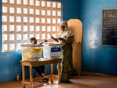 In a blue, sunlit room, a woman casts her vote in the Sierra Leone presidential election