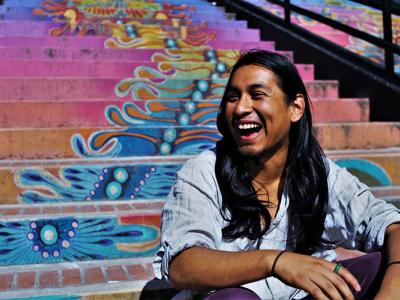 Jesus Nazario, a Ph.D. student in ethnic studies, sitting on a colorful outdoor stairway and smiling.