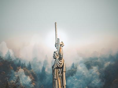 a steel statue of a person holding a sword with trees and fog in the background