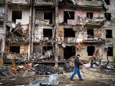 a lone man in a hat and jeans walks past a building complex shattered by Russian missiles in Kyiv, Ukraine