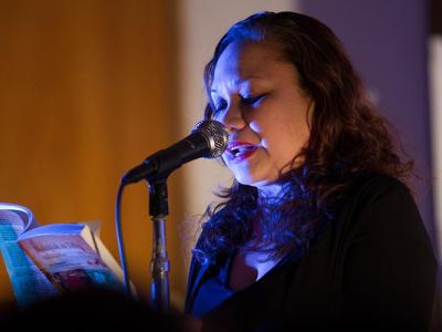 Joie Barrios-Leblanc reading a poem at a microphone.