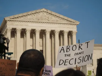 People standing in front of the U.S. Supreme Court. A sign is shown saying "Abort the draft decision."