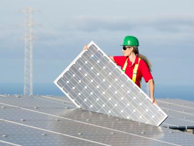 a worker in a green hardhat carries a solar panel for installation