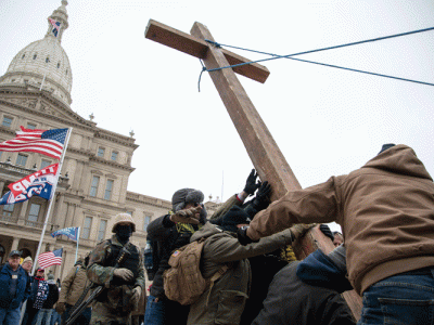 Members of right-wing extremist Proud Boys group raised a wooden cross outside the state capitol building in Lansing, Michigan, on Jan. 6, 2021. An American flag and a Trump flag are in the background.