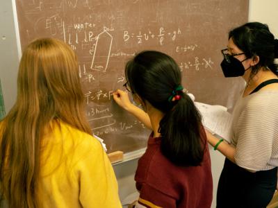 3 women at a chalkboard with masks