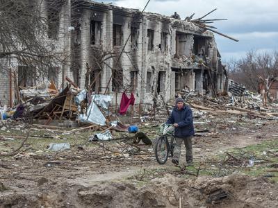 a person walks a bicycle by a destroyed building