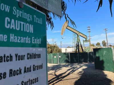 A photo shows an oil rig located in a neighborhood in Los Angeles. In the foreground is a sign for a city park.