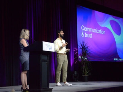 two people standing on a dark stage for a presentation in front of a screen that says "communication and trust."
