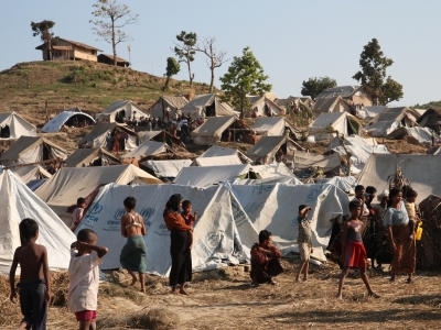 Burmese families with little children standing in front of white tents in a rural area.