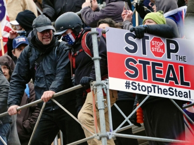 A mob of men, some wearing assault gear, pass by a "stop the steal" placard as they attack US capitol