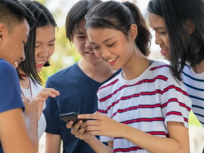 Smiling Asian youth clustered around one with phone in hand